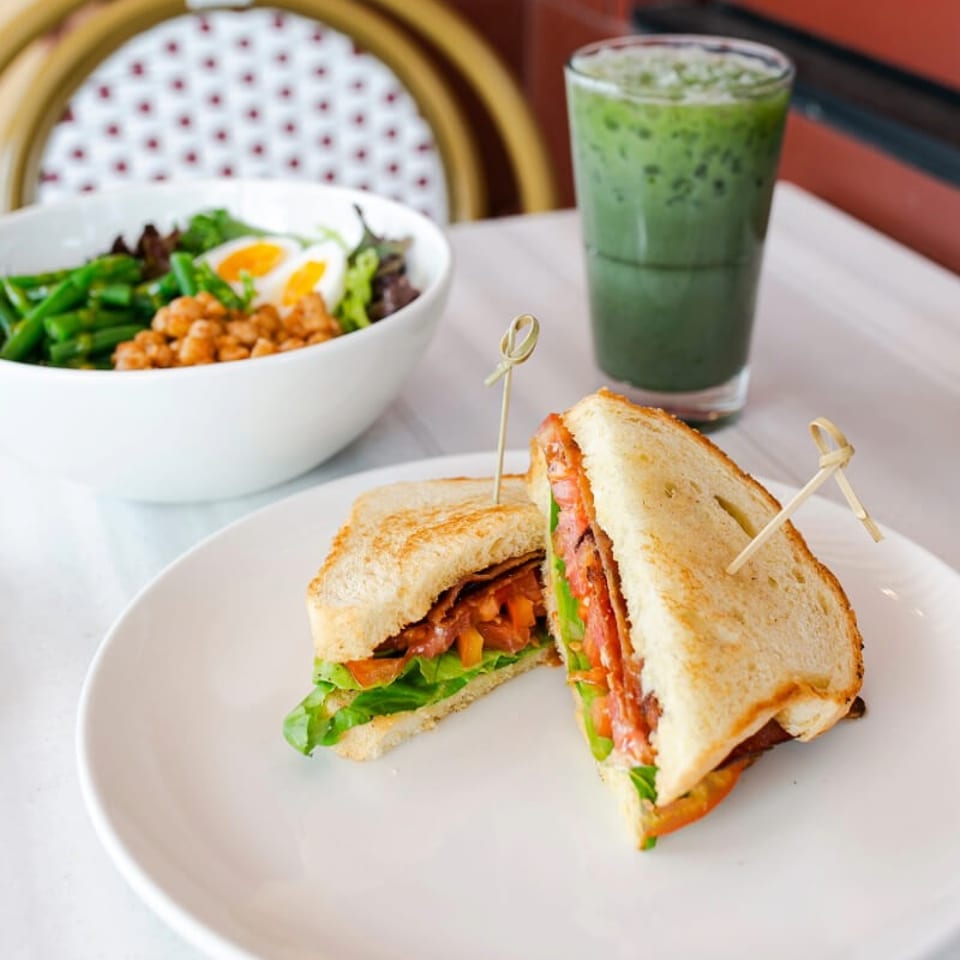 Grilled sandwich halves with lettuce and tomato, a green iced drink, and a salad bowl on a restaurant table.