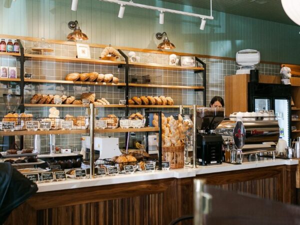 The interior service counter and bread shelves of Le Rouge Bakery, featuring fresh loaves, pastry baskets, and an espresso machine.