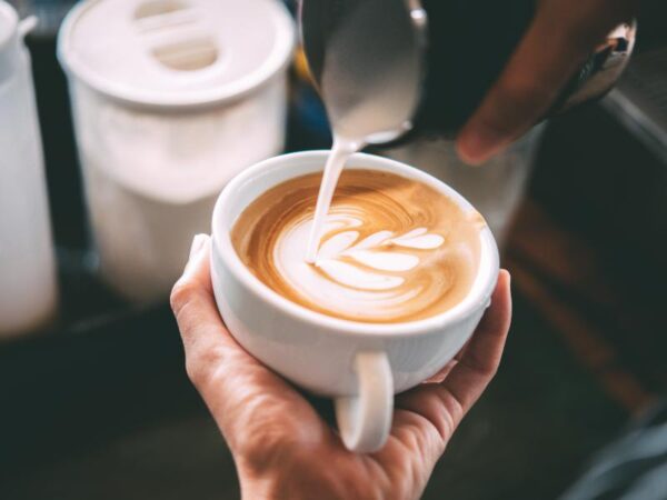 Barista pouring steamed milk into the cappuccino to create tulip art at Le Rouge Bakery.