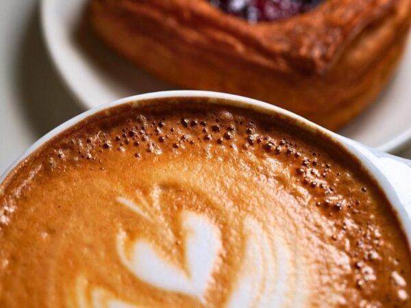 Close-up of a frothy cappuccino with heart latte art and delicate bubbles, served alongside a berry Danish pastry at Le Rouge Bakery.