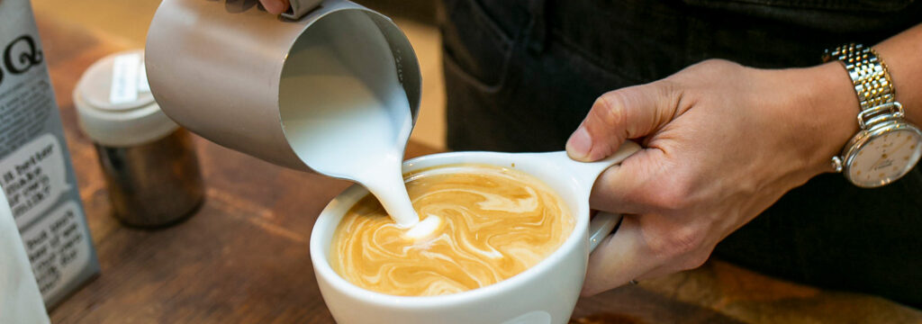 Barista pouring steamed milk into a freshly brewed latte at LeRouge French cafe.